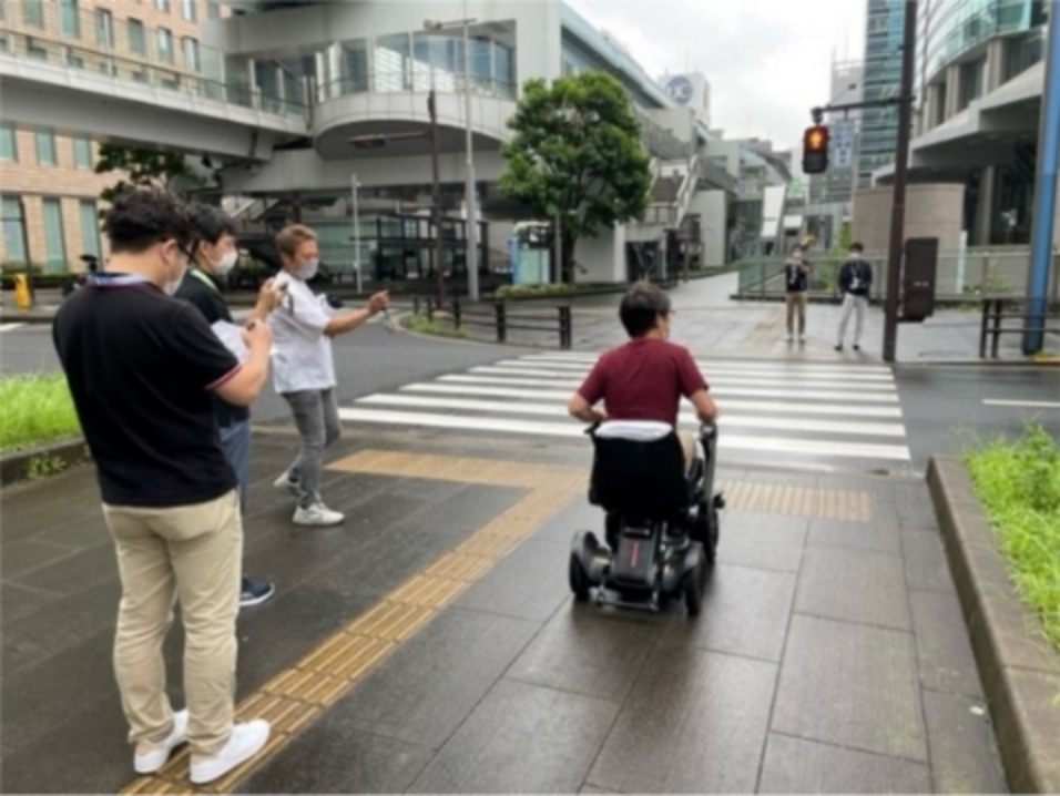 Photo: Checking the accessibility of a crosswalk. The photo shows an employee using an electric wheelchair, with other employees taking pictures and making notes.