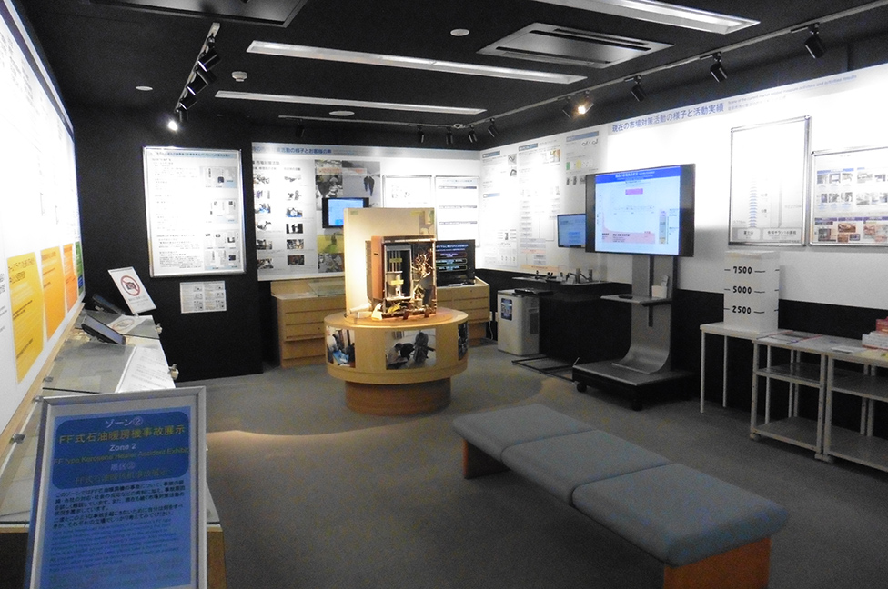 Photo of the Product Safety Learning Square, featuring a gray three-seat sofa at the center and walls displaying numerous product safety panels and educational materials.