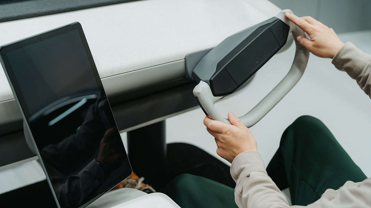 ハンドルを握る人物、タブレット端末が置かれたコンソール、近未来的なデザイン、運転席