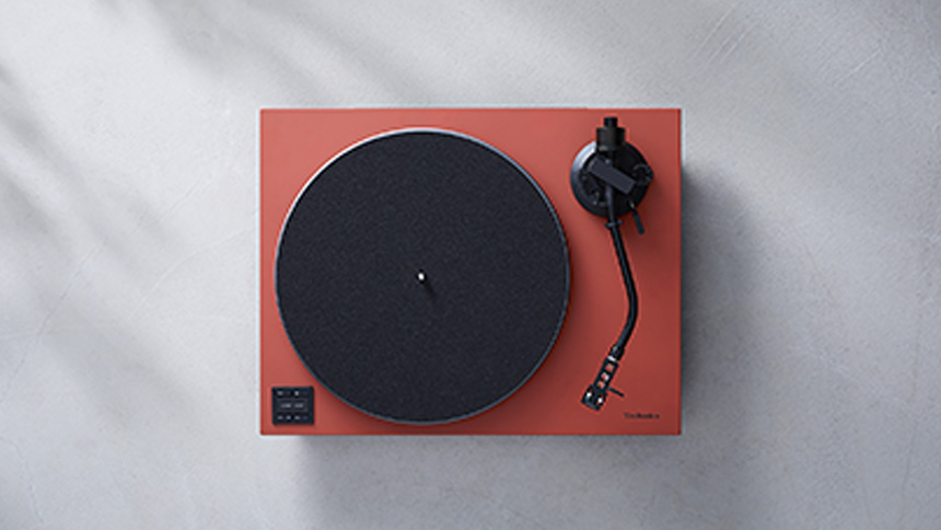 赤いレコードプレーヤーの上面、黒い円形ターンテーブルとトーンアーム