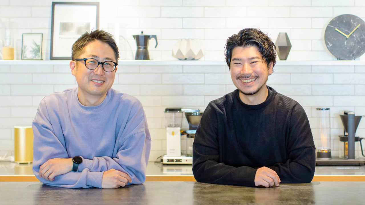 男性二人がカウンター越しに笑顔でこちらを向いている