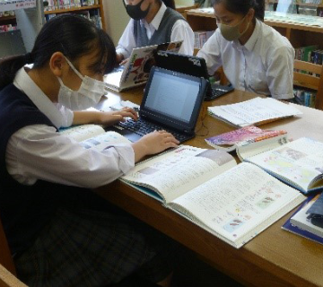 小論文作成のためパソコンや本を使って調べる女子生徒の様子