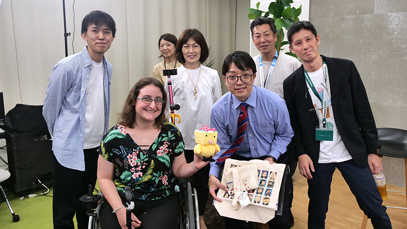 写真：笑顔で記念撮影をする登壇者たち。うち1人は車椅子に座っている