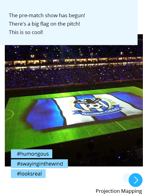 Photo: A huge flag created by projection mapping appears on the stadium pitch. Post: The pre-match show has begun! There's a big flag on the pitch! This is so cool! Hashtags: #humongous #swayinginthewind #looksreal "Projection Mapping"