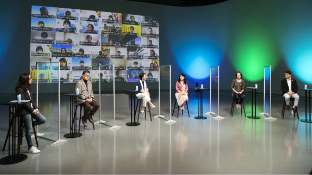 Photo: Group DEI Forum 2021. The moderator and five speakers are seated in the studio, with many faces of employees participating online on a large screen in the background.