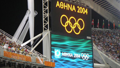 照片：设置在雅典奥运会会场的大型影像显示装置ASTRO VISION上显示的五环标志和雅典奥运会会徽