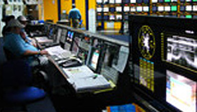 写真：アテネオリンピックIBC（国際放送センター）のメインコントロール室で多数のモニターを使用し人々が作業している様子