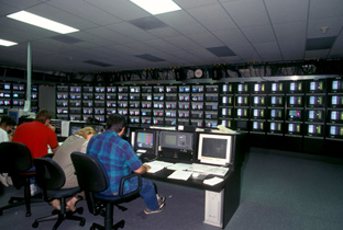 照片：在IBC（国际广播中心），工作人员使用多台显示器和播放设备进行工作的情景