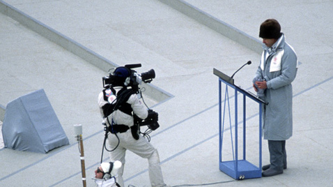 写真：カルガリー冬季オリンピックの開会式セレモニーでスピーチをしている人を放送カメラマンが撮影している様子