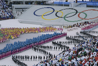 照片：在卡尔加里冬季奥运会开幕式上，描绘在看台上的五轮标志和穿着鲜艳服装的人们在体育场中央区域进行的舞蹈表演
