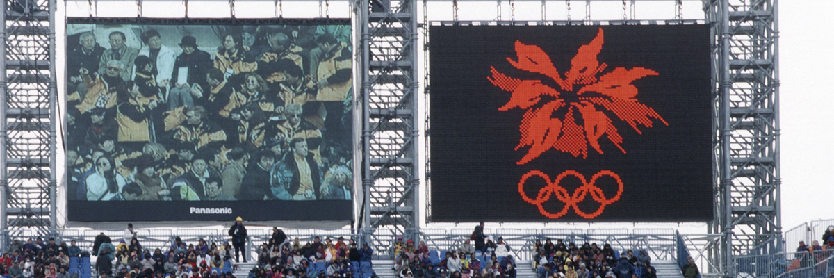 照片：设置在长野冬季奥运会开幕式会场的2台大型影像显示装置ASTRO VISION上显示的观众席画面及长野冬季奥运会会徽
