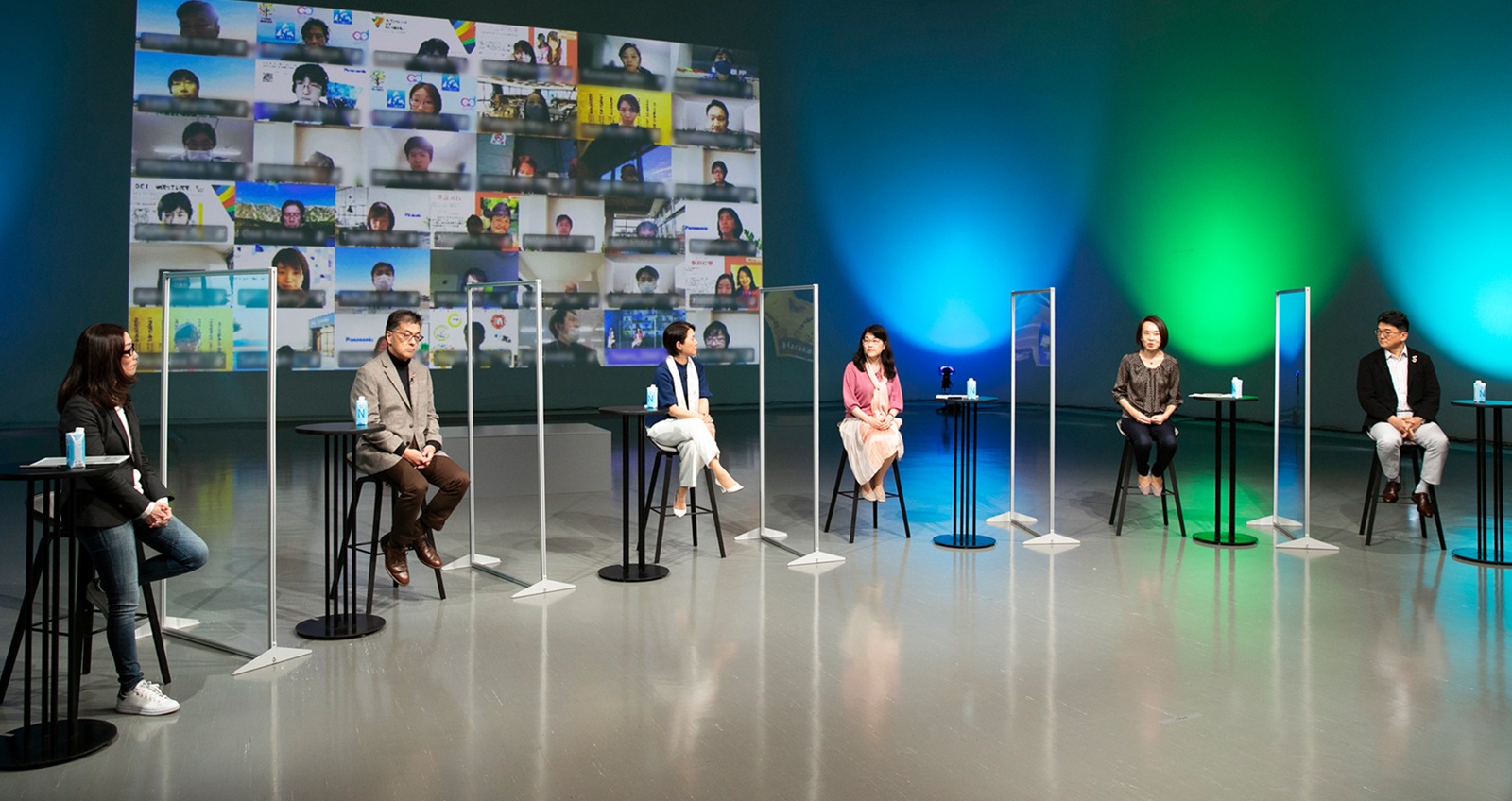 写真：「グループDEIフォーラム 2021」の様子。スタジオに司会者と5人の登壇者が着席し、背景にある大きなスクリーンにオンライン参加の社員の顔が複数並んでいる。