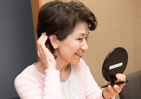 写真：充電式耳かけ型補聴器をつけた感じを確認する女性